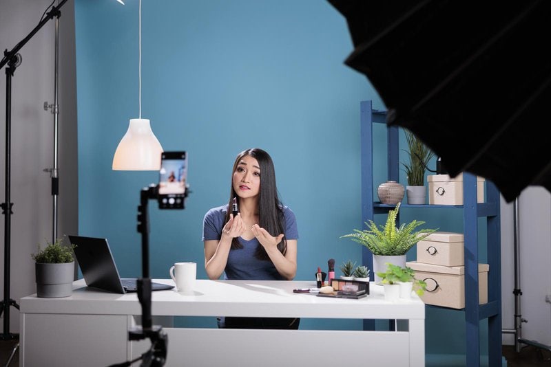 Social media content creator holding lipstick doing makeup review for vlogging channel advertising cosmetic product. Behind the scene of asian woman recording make up tutorial in studio