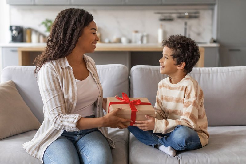Excited Black Woman Receiving Present For Mother's Day From Her Little Son, Cute African American Male Kid Surprising Mom With Gift While They Spending Time Together At Home, Free Space