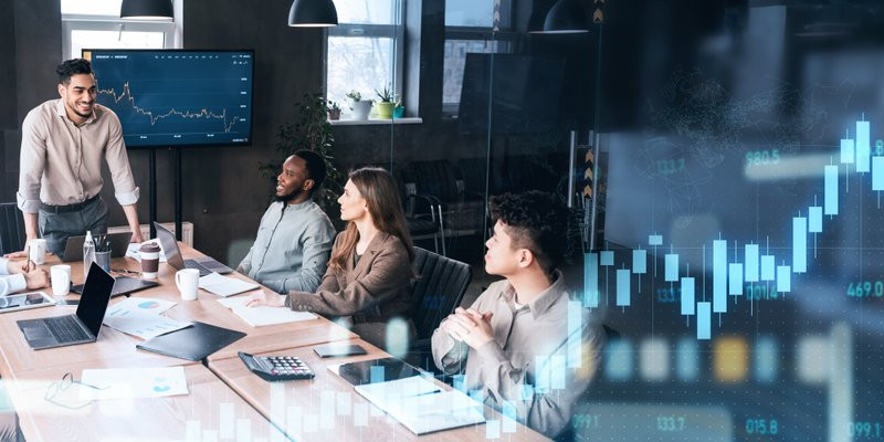 Energetic team leader stands addressing his attentive colleagues during a collaborative meeting in a modern workspace, with digital stock market data overlay, panorama. Work, business
